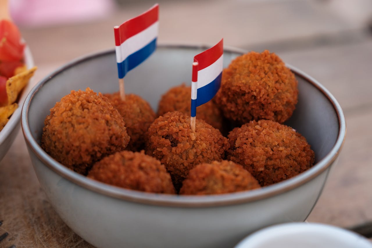 Close-up of Dutch bitterballen in a ceramic bowl with mini flags, on an outdoor cafe terrace.